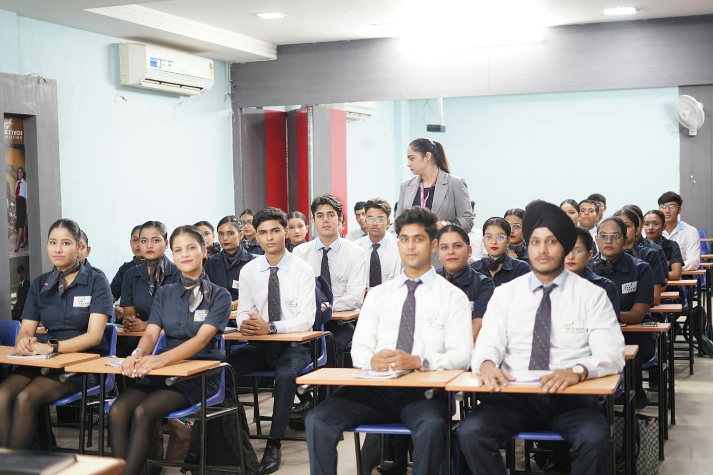 Students in uniforms sit at desks while an instructor observes.