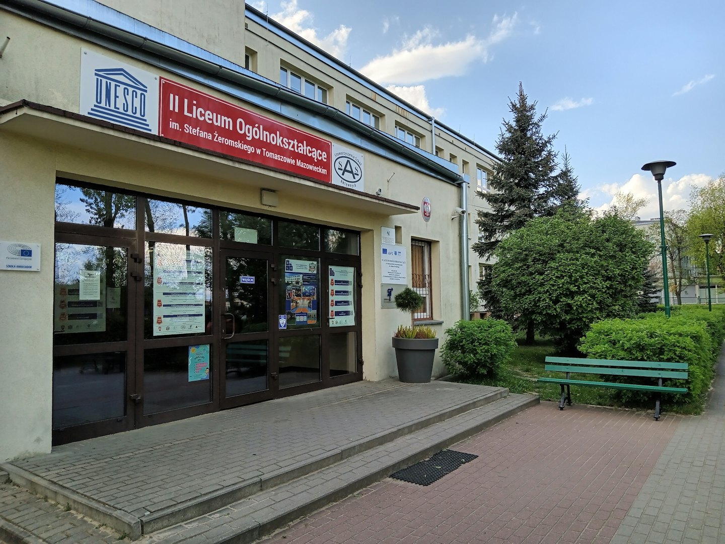 Two-story school entrance with glass doors and a wooden bench.