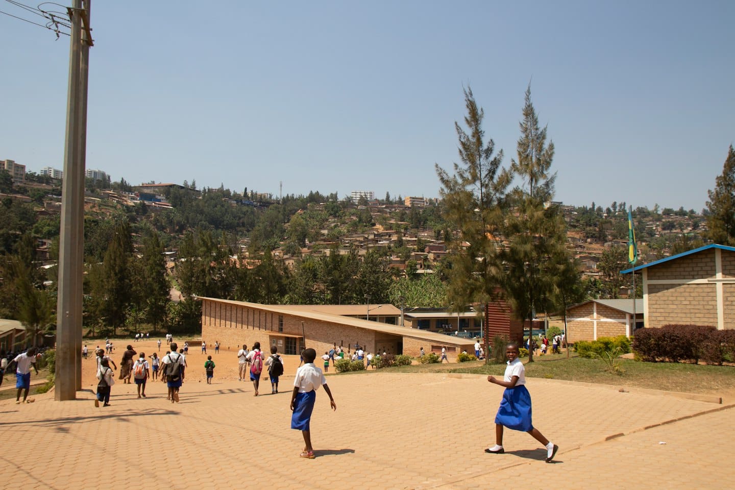 African schoolchildren in uniform run across a sunny schoolyard.